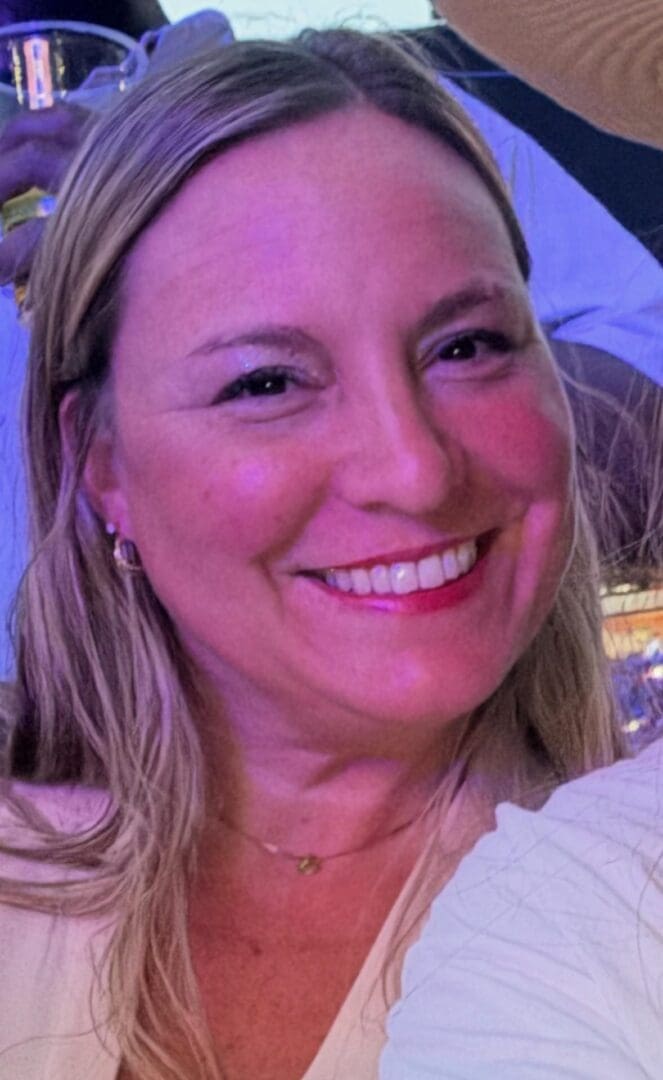 Smiling woman with blonde hair in a warmly lit setting.