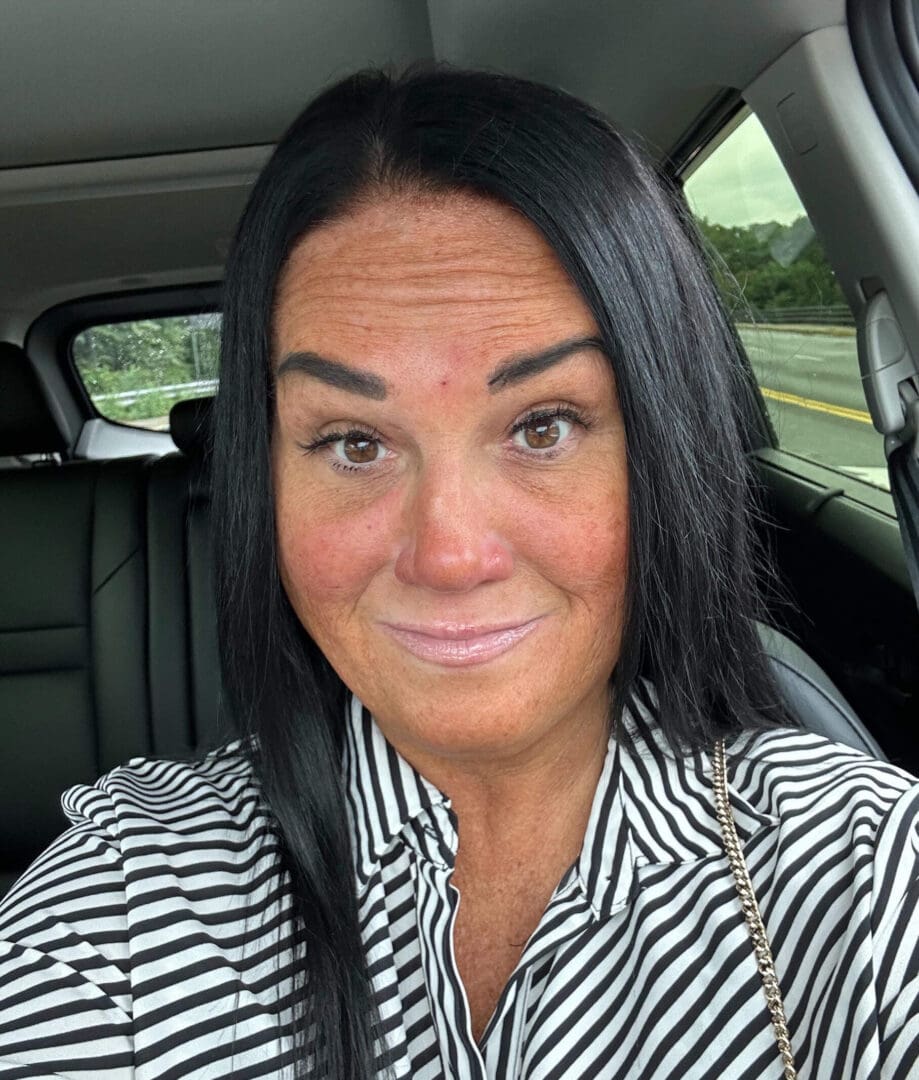 Woman with long black hair sitting in a car wearing a striped top.