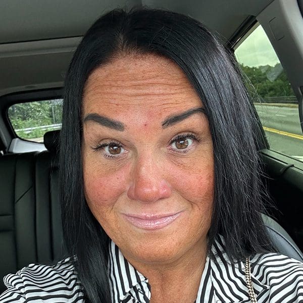 Woman with dark hair smiling inside a car.