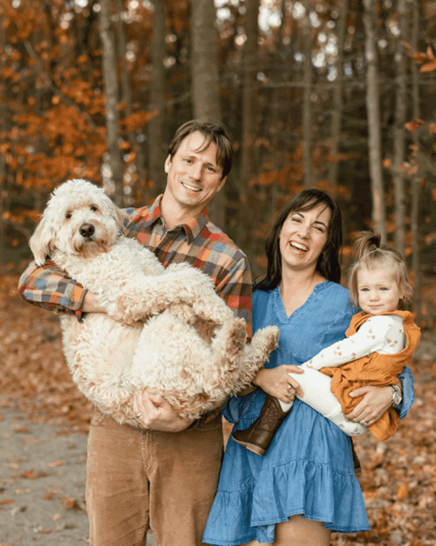 A happy family holding their dogs in a forest during autumn.